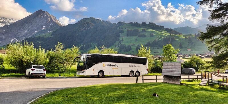 Bílý autobus Setra Umbrella Travel u louky pod horami v Alpách
